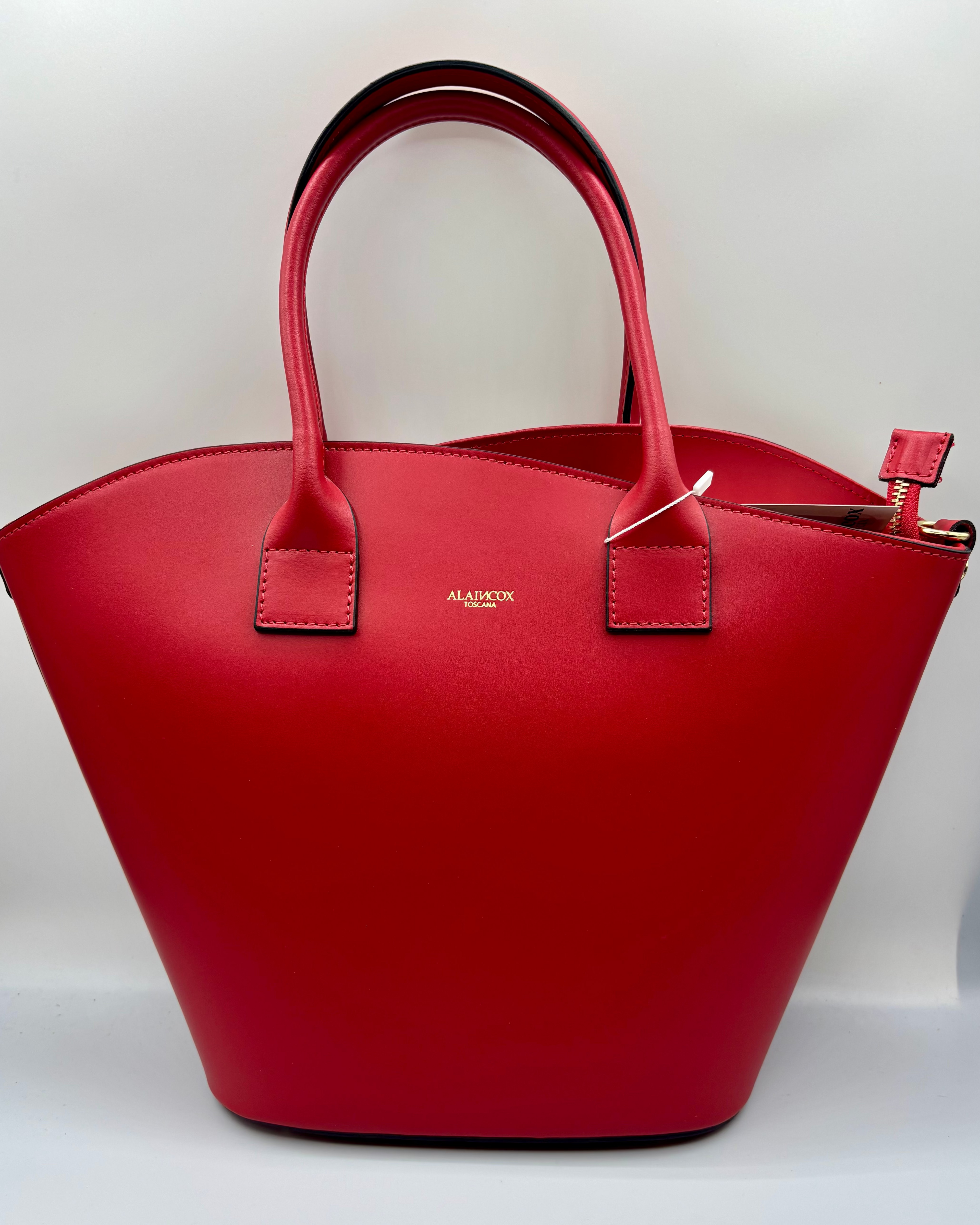 La Borsa Siviglia di ALAINCOX in vera pelle liscia Made in Italy, elegante e spaziosa, con design rosso intenso, chiusura a zip, hardware dorato e tracolla regolabile. Disponibile a Genova nel negozio ALAINCOX in Via di Fossatello. Perfetta per l’uso quotidiano grazie alle dimensioni capienti 38×27×12 cm.