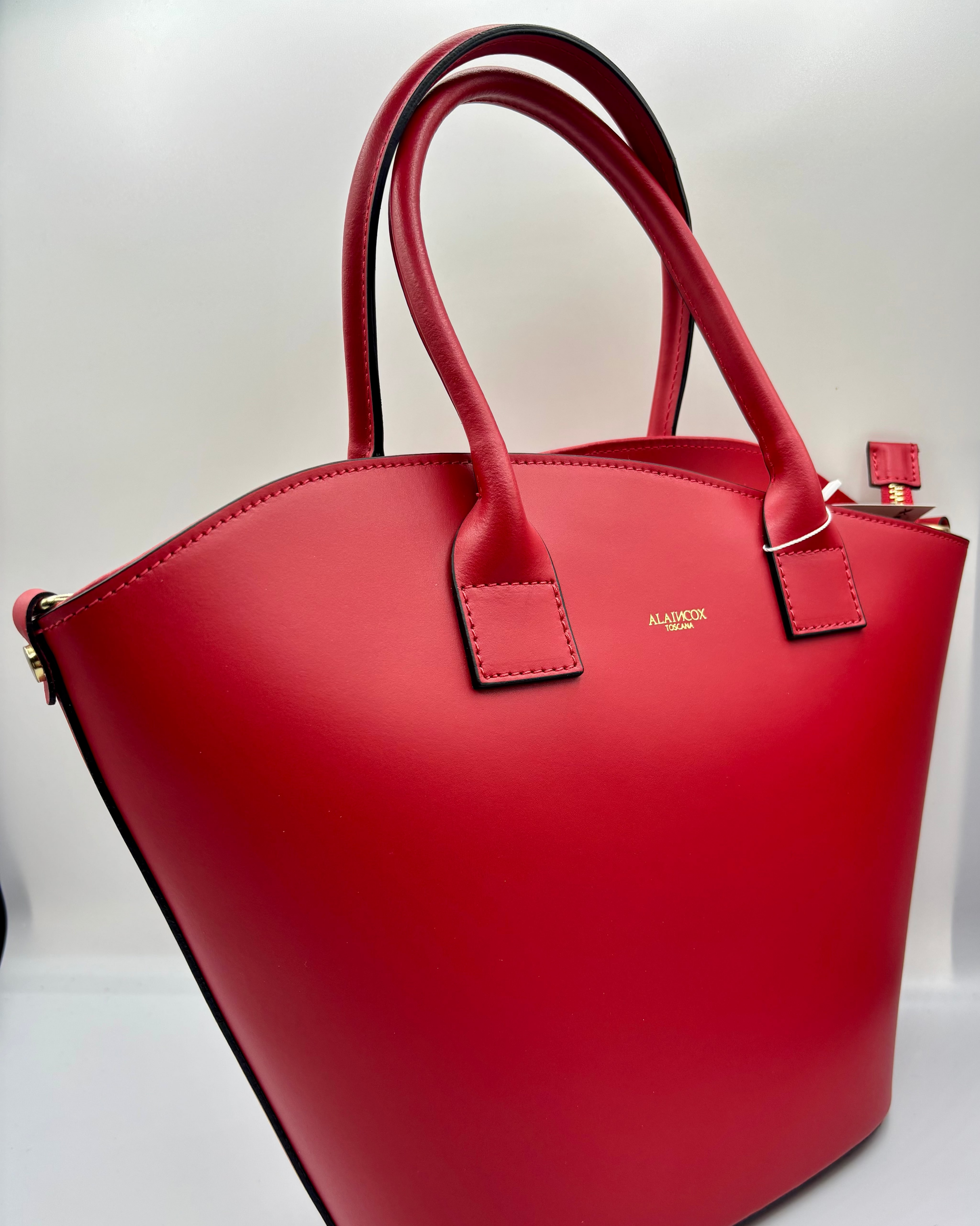 La Borsa Siviglia di ALAINCOX in vera pelle liscia Made in Italy, elegante e spaziosa, con design rosso intenso, chiusura a zip, hardware dorato e tracolla regolabile. Disponibile a Genova nel negozio ALAINCOX in Via di Fossatello. Perfetta per l’uso quotidiano grazie alle dimensioni capienti 38×27×12 cm.